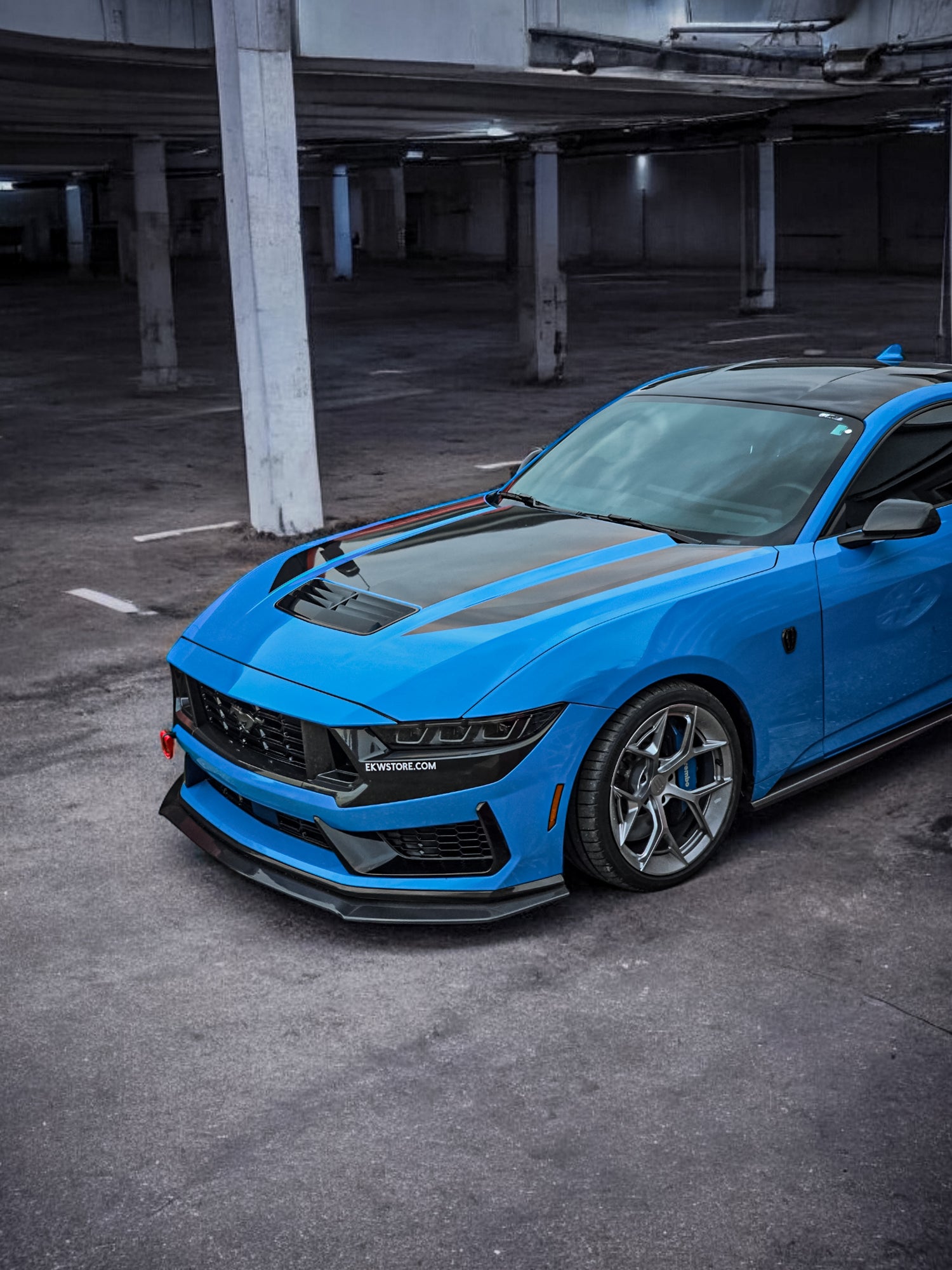Blue Ford Mustang Dark Horse with EKW wheels, aggressive aero upgrades, and a black vented hood, parked in an industrial-style garage. Shop high-performance wheels and carbon fiber parts at EKWSTORE.COM.