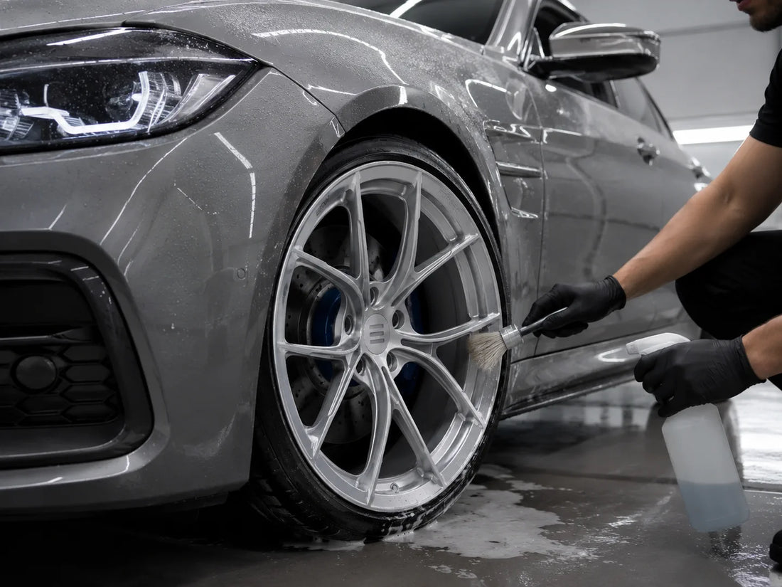 Detailer cleaning a silver EKW LYN-1 forged wheel on a gray BMW performance sedan in a premium studio